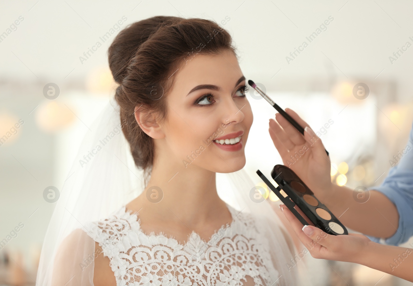 Photo of Makeup artist preparing bride before her wedding in room