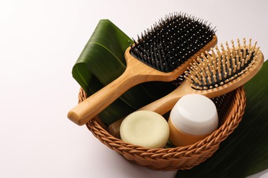 Photo of Wicker basket with wooden hairbrushes, cosmetic products and green leaves on white background