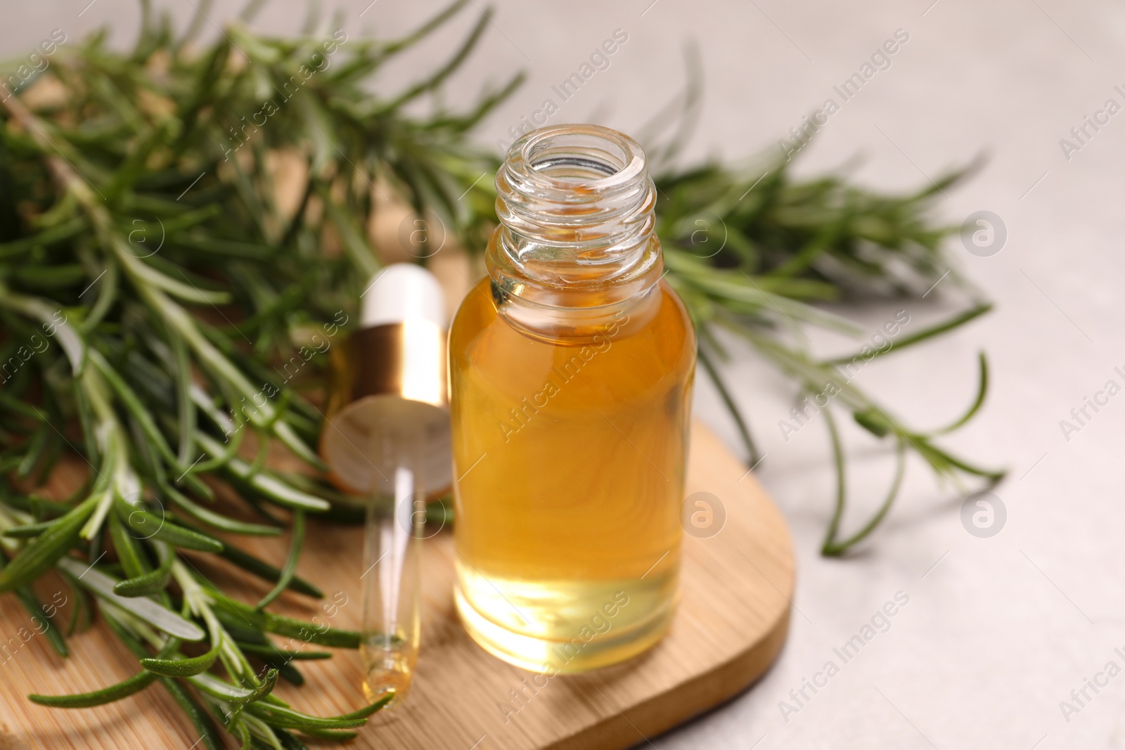 Photo of Bottle of essential oil and fresh rosemary on light grey table, closeup