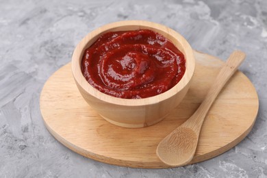 Photo of Organic ketchup in wooden bowl and spoon on grey textured table. Tomato sauce