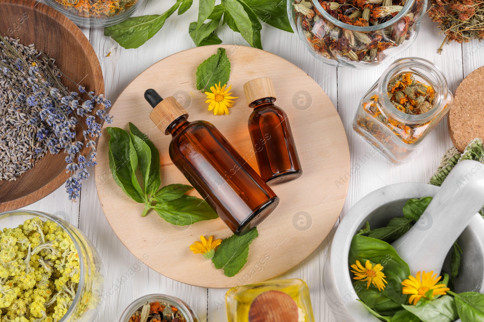 Photo of Bottles of essential oils surrounded by different herbs on white wooden table, flat lay