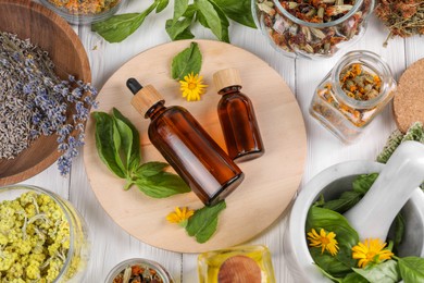 Bottles of essential oils surrounded by different herbs on white wooden table, flat lay