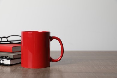 Photo of Red ceramic mug, stationery and glasses on wooden table, space for text