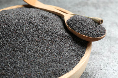 Photo of Wooden bowl and spoon with poppy seeds on grey table, closeup