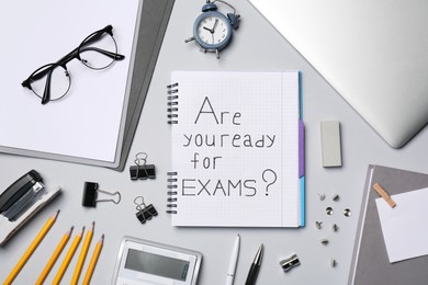 Photo of Notebook with question Are you ready for exams and stationery on grey table, flat lay