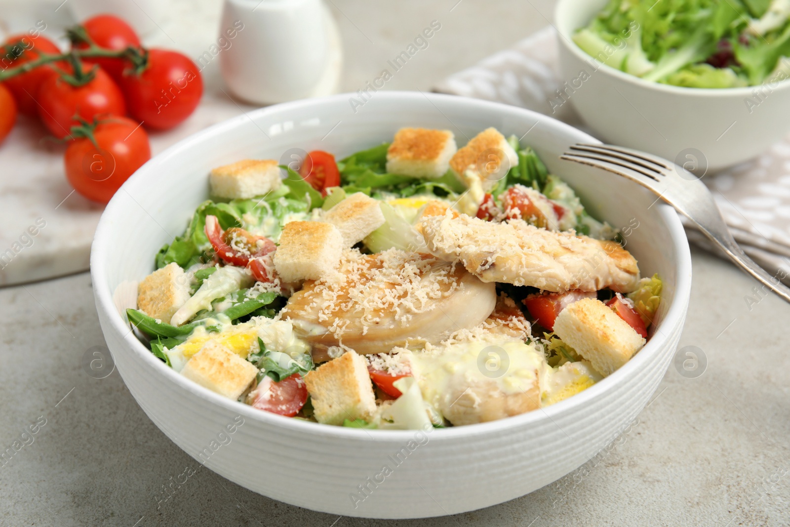 Photo of Delicious fresh Caesar salad in bowl on light grey table, closeup