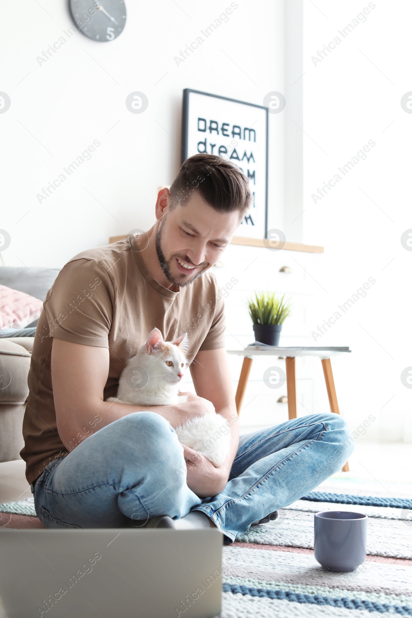 Photo of Young man with cute cat and laptop at home