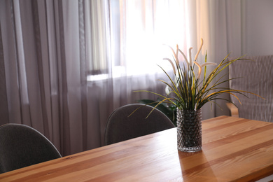 Photo of Vase on wooden table near window with curtains in room