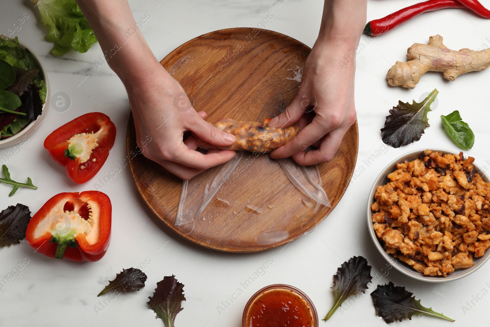 Photo of Woman making tasty spring roll at white marble table, top view