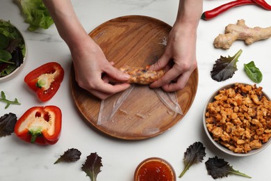 Photo of Woman making tasty spring roll at white marble table, top view