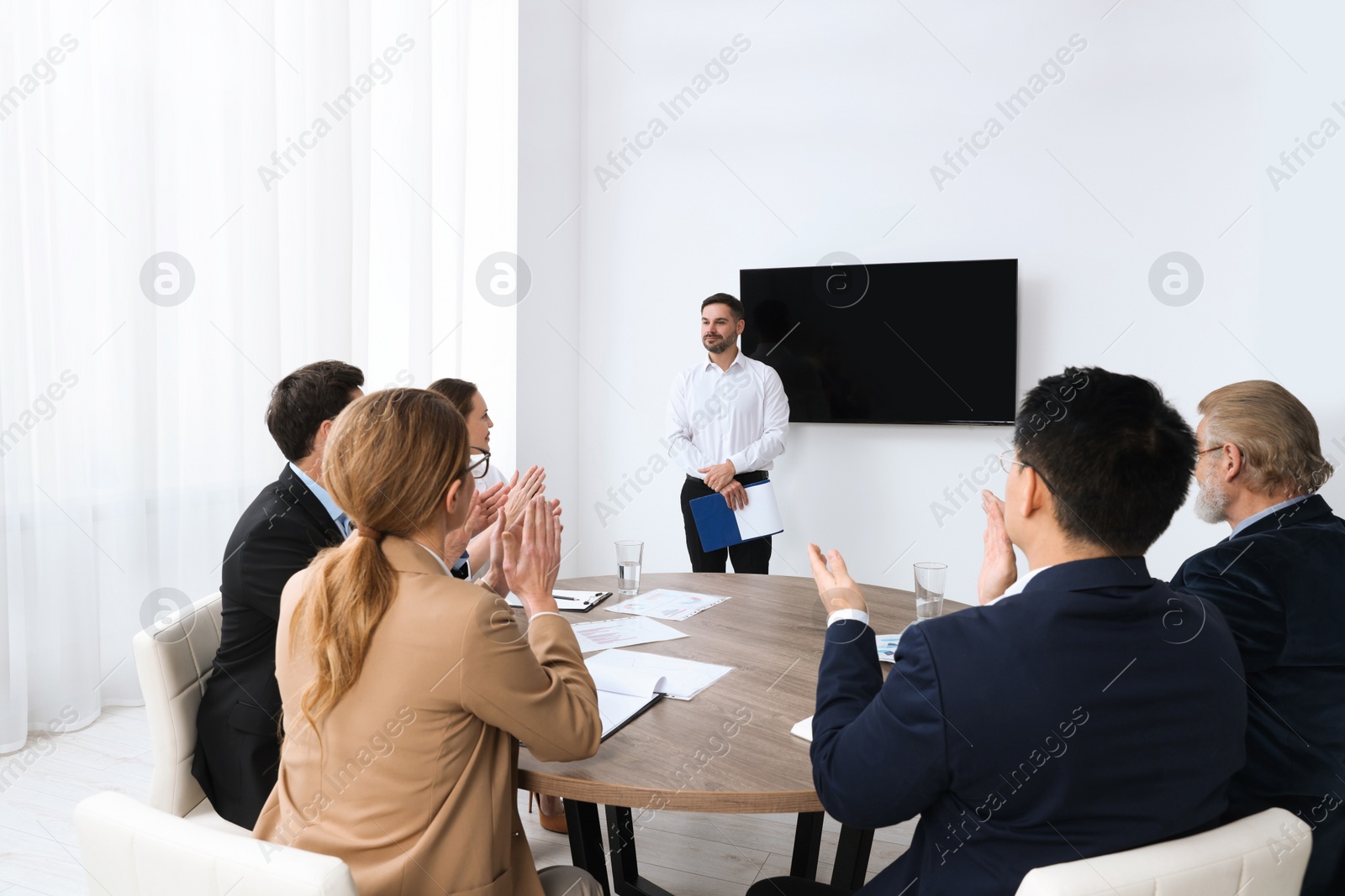 Photo of Business conference. Group of people listening to speaker report near tv screen in meeting room