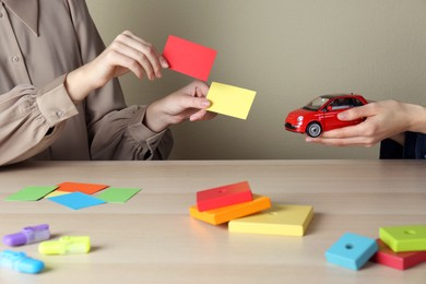 Photo of Women with toy car and color papers at wooden table indoors, closeup. ABA therapy concept
