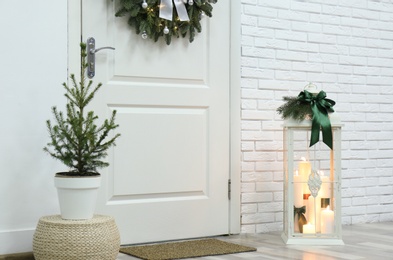 Photo of Beautiful Christmas lantern and potted fir tree near entrance indoors