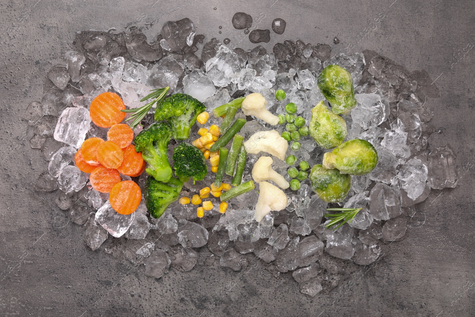 Photo of Different frozen vegetables with ice on grey textured table, top view