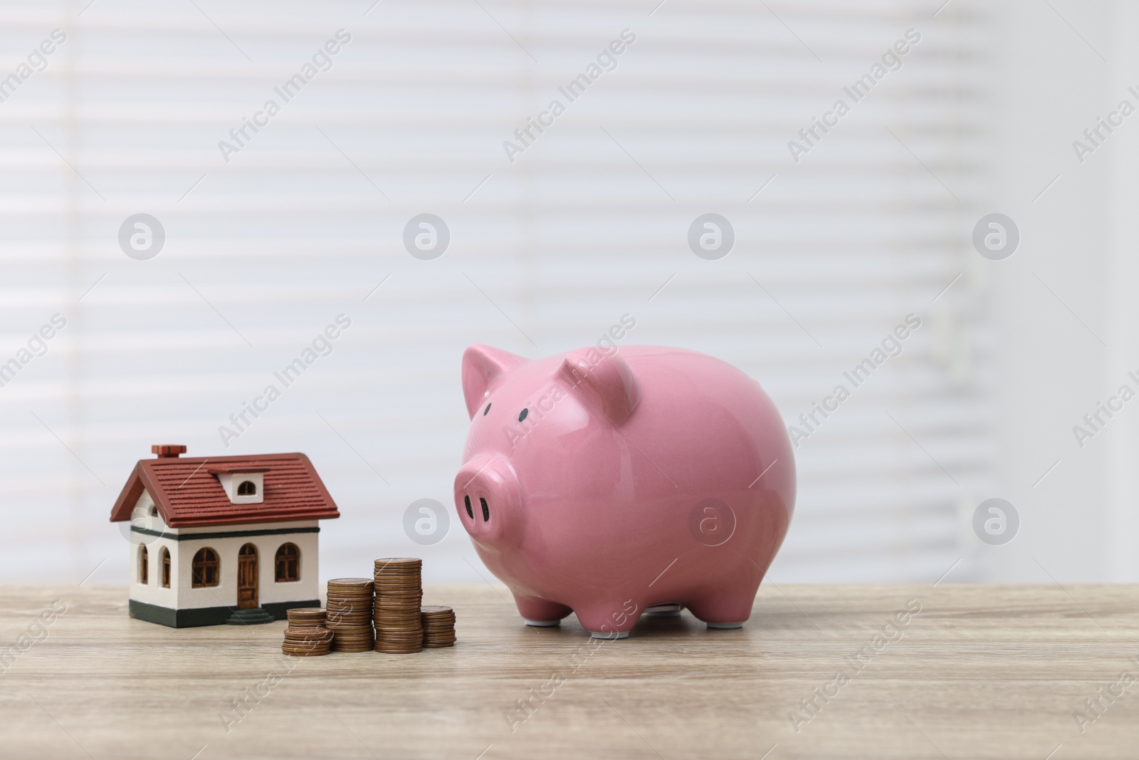 Photo of House model, piggy bank and stacked coins on wooden table