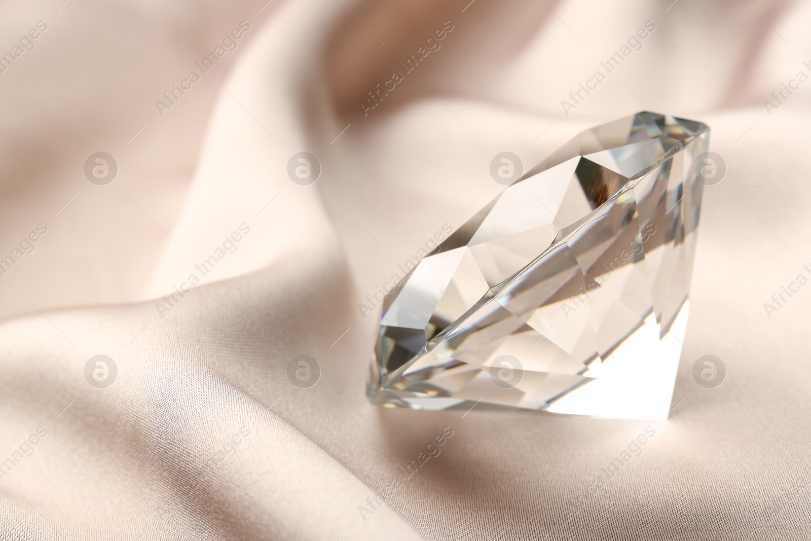Photo of Beautiful shiny diamond on beige silky fabric, closeup. Space for text