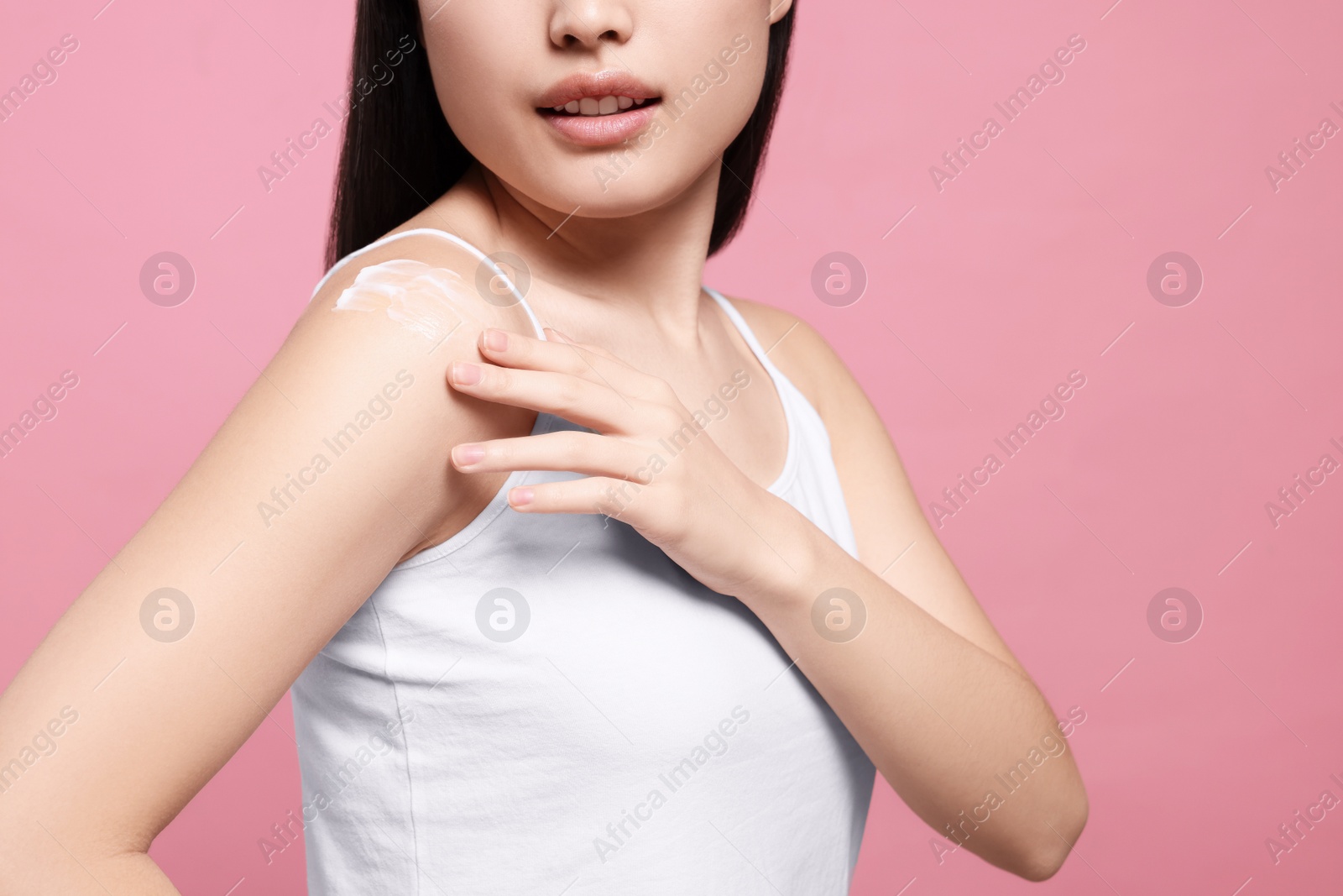 Photo of Young woman applying body cream onto shoulder on pink background, closeup. Space for text