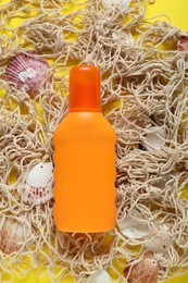 Bottle of suntan cream, seashells and net on yellow background, flat lay