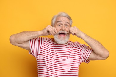 Senior man touching mustache on orange background