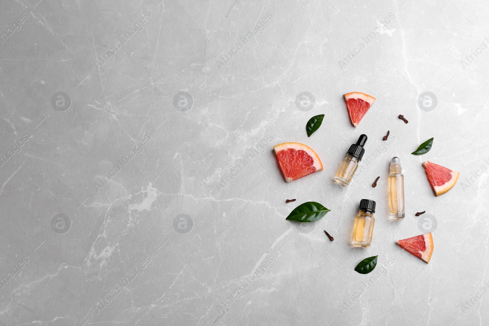 Photo of Flat lay composition with grapefruit slices and bottles of essential oil on grey background, space for text