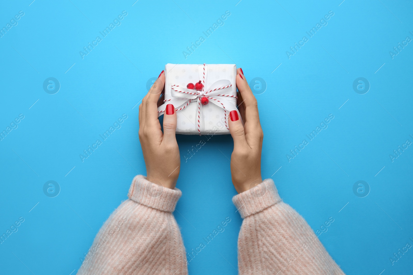 Photo of Woman holding Christmas gift box on light blue background, top view