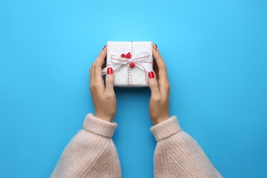 Photo of Woman holding Christmas gift box on light blue background, top view