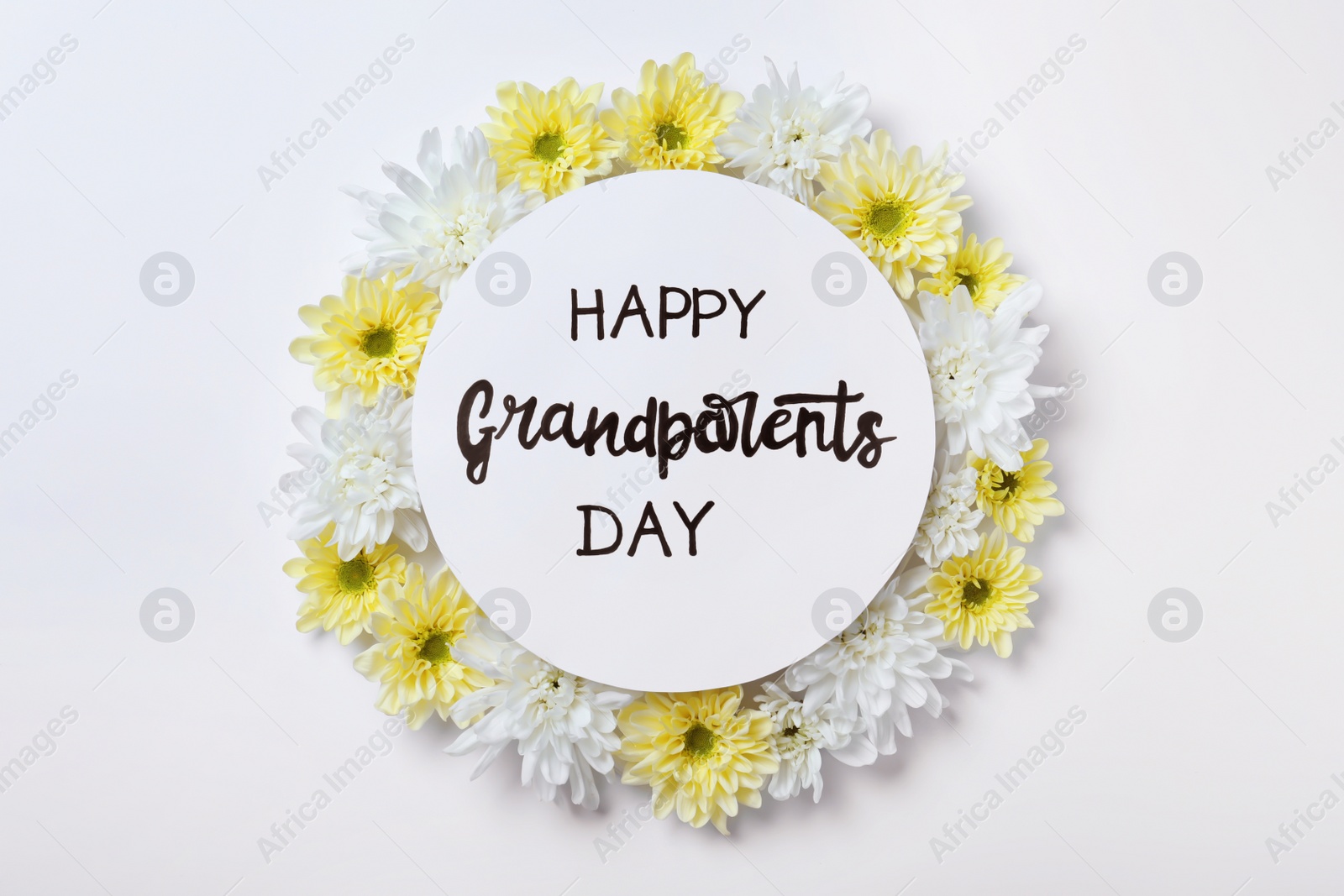 Photo of Card with phrase Happy Grandparents Day and beautiful flowers on white background, flat lay