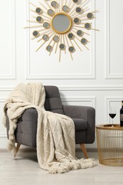 Photo of Comfortable armchair, blanket and wine on side table near white wall. Interior design