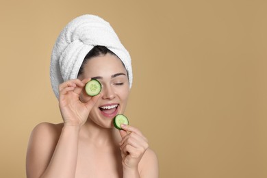 Photo of Woman with towel holding pieces of cucumber on beige background, space for text. Spa treatment