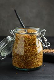 Whole grain mustard and spoon in jar on black wooden table