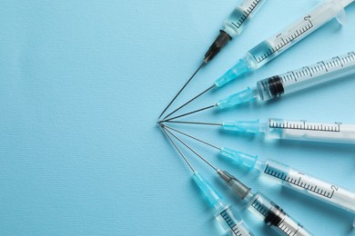 Disposable syringes with needles and medicine on light blue background, flat lay. Space for text