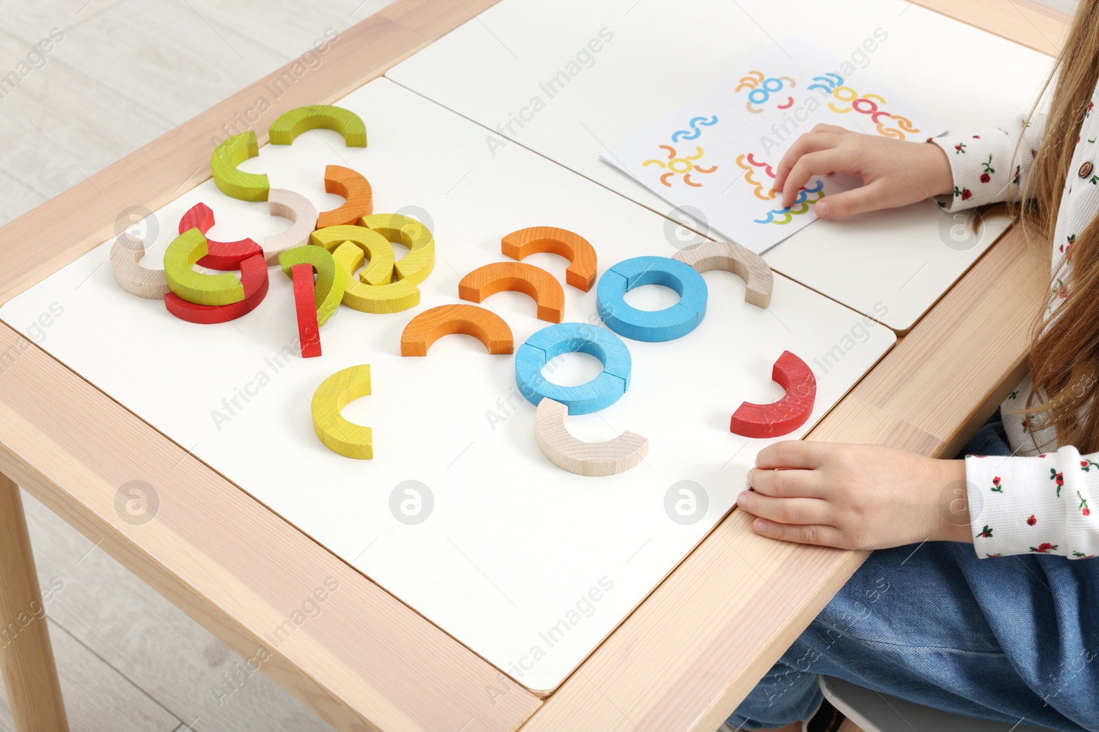 Photo of Motor skills development. Girl playing with colorful wooden arcs at white table indoors, closeup