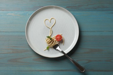 Photo of Heart made of tasty spaghetti, fork and tomato on light blue wooden table, top view