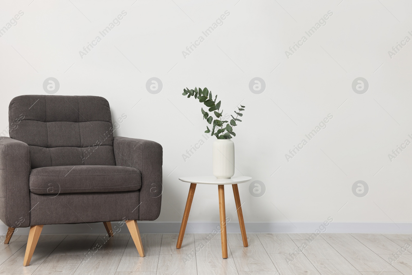 Photo of Comfortable armchair, side table and eucalyptus near white wall indoors, space for text