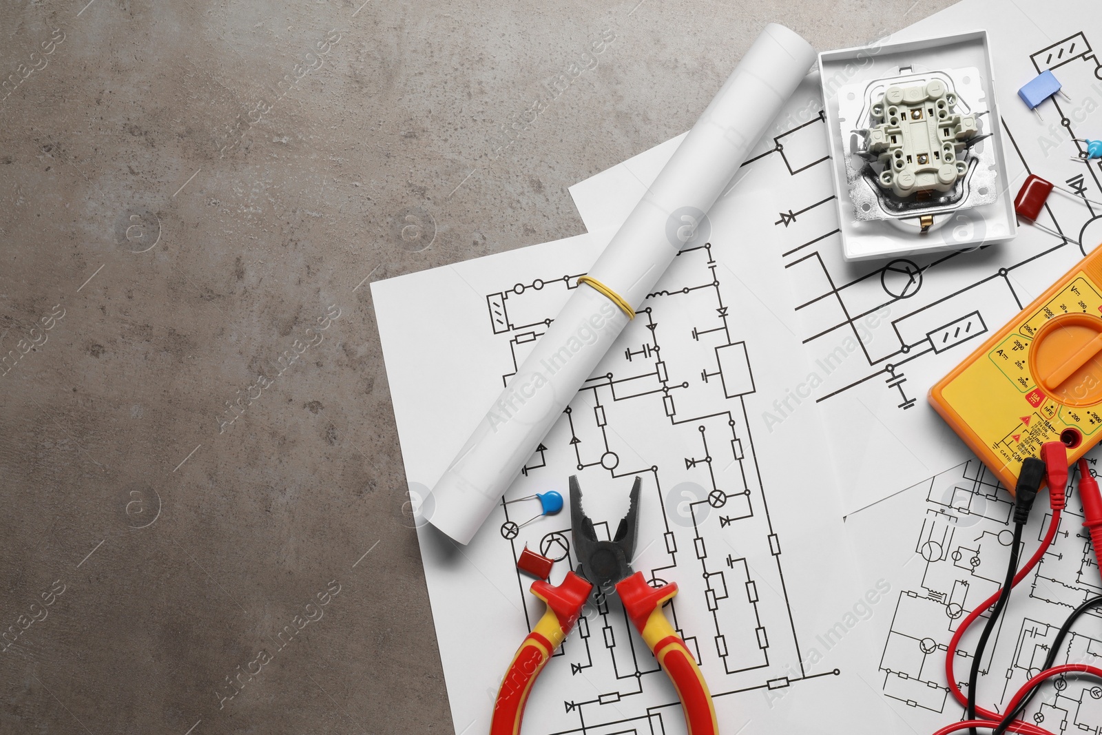 Photo of Wiring diagrams, digital multimeter and other electrician's equipment on grey table, top view. Space for text