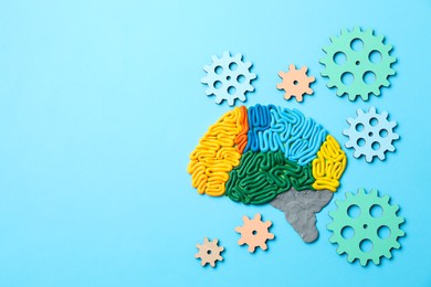 Photo of Amnesia problem. Brain with sections made of plasticine and gears on light blue background, flat lay. Space for text