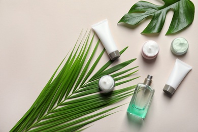 Photo of Different skin care cosmetic products with green leaves on light background, top view