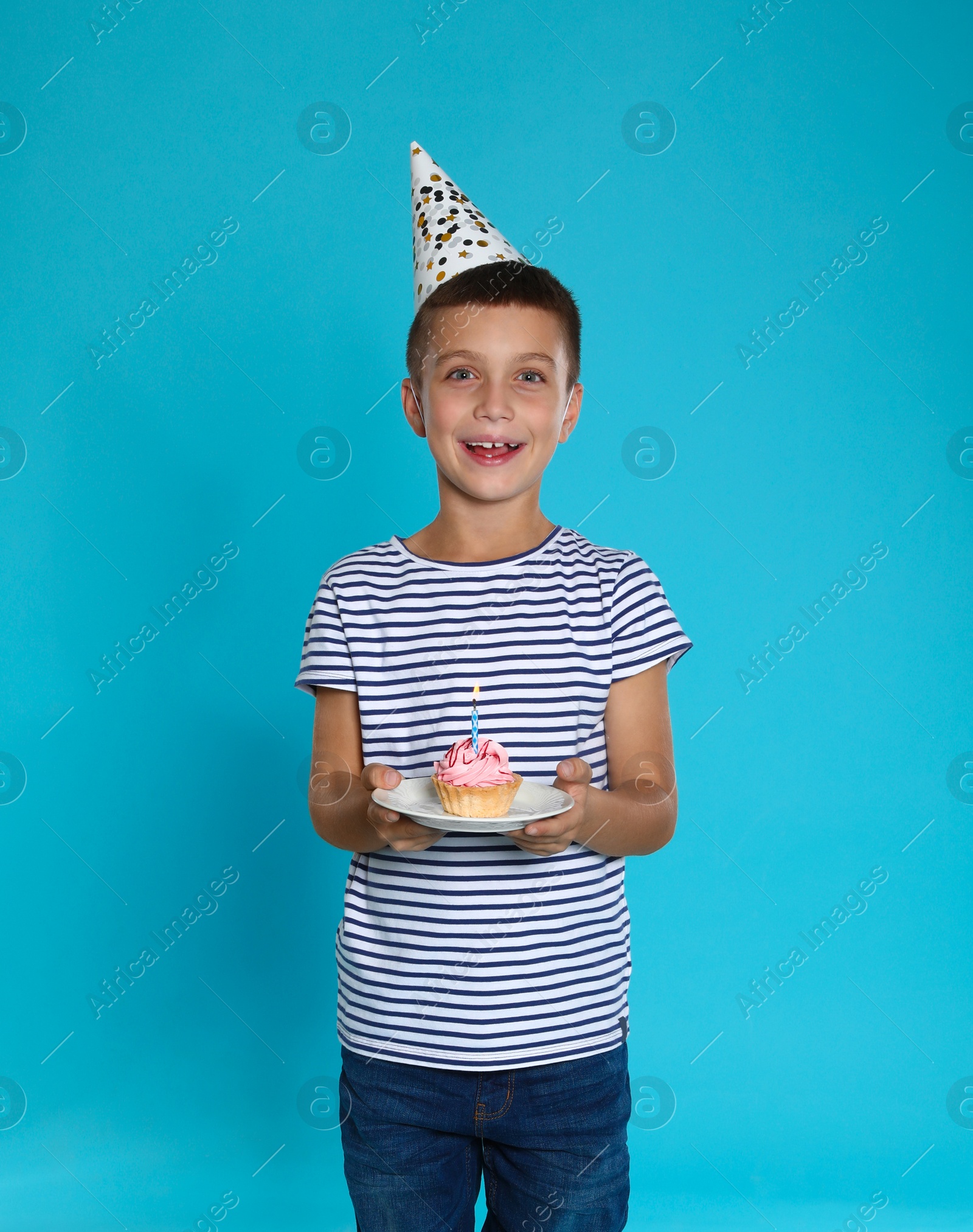Photo of Happy boy holding birthday cupcake with candle on blue background