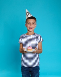 Happy boy holding birthday cupcake with candle on blue background