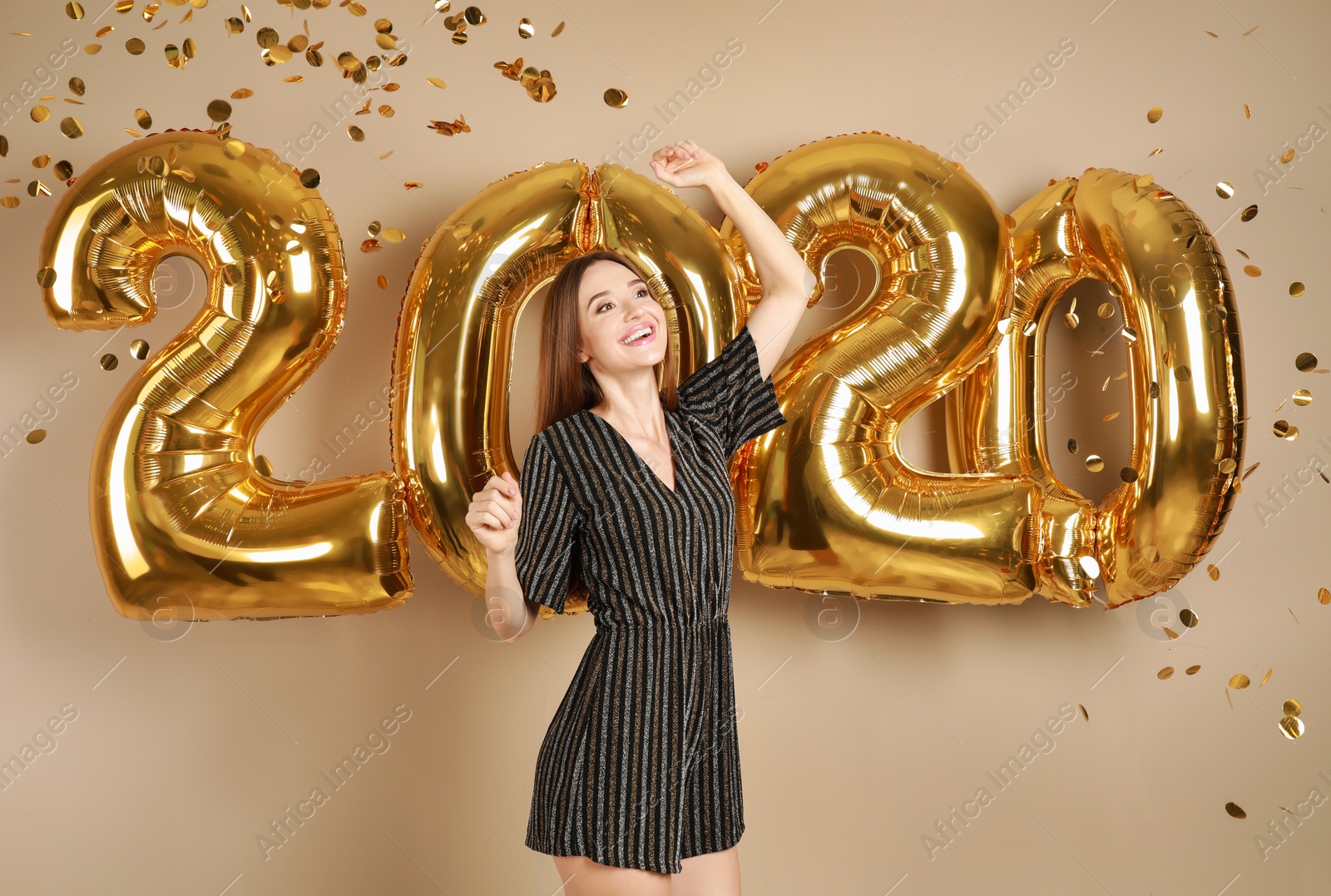 Photo of Excited young woman near golden 2020 balloons on beige background. New Year celebration