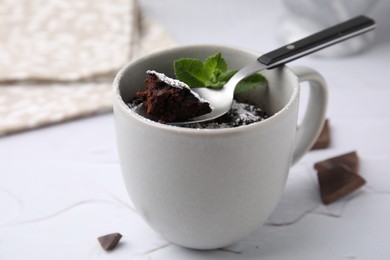 Photo of Tasty chocolate mug pie with mint and spoon on white table, closeup. Microwave cake recipe