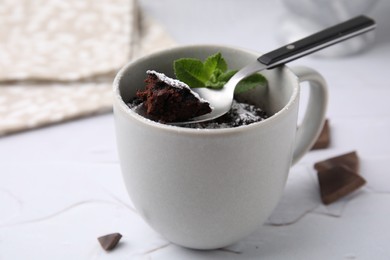 Tasty chocolate mug pie with mint and spoon on white table, closeup. Microwave cake recipe