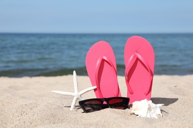 Stylish pink flip flops, sunglasses, starfish and seashell on beach sand, space for text