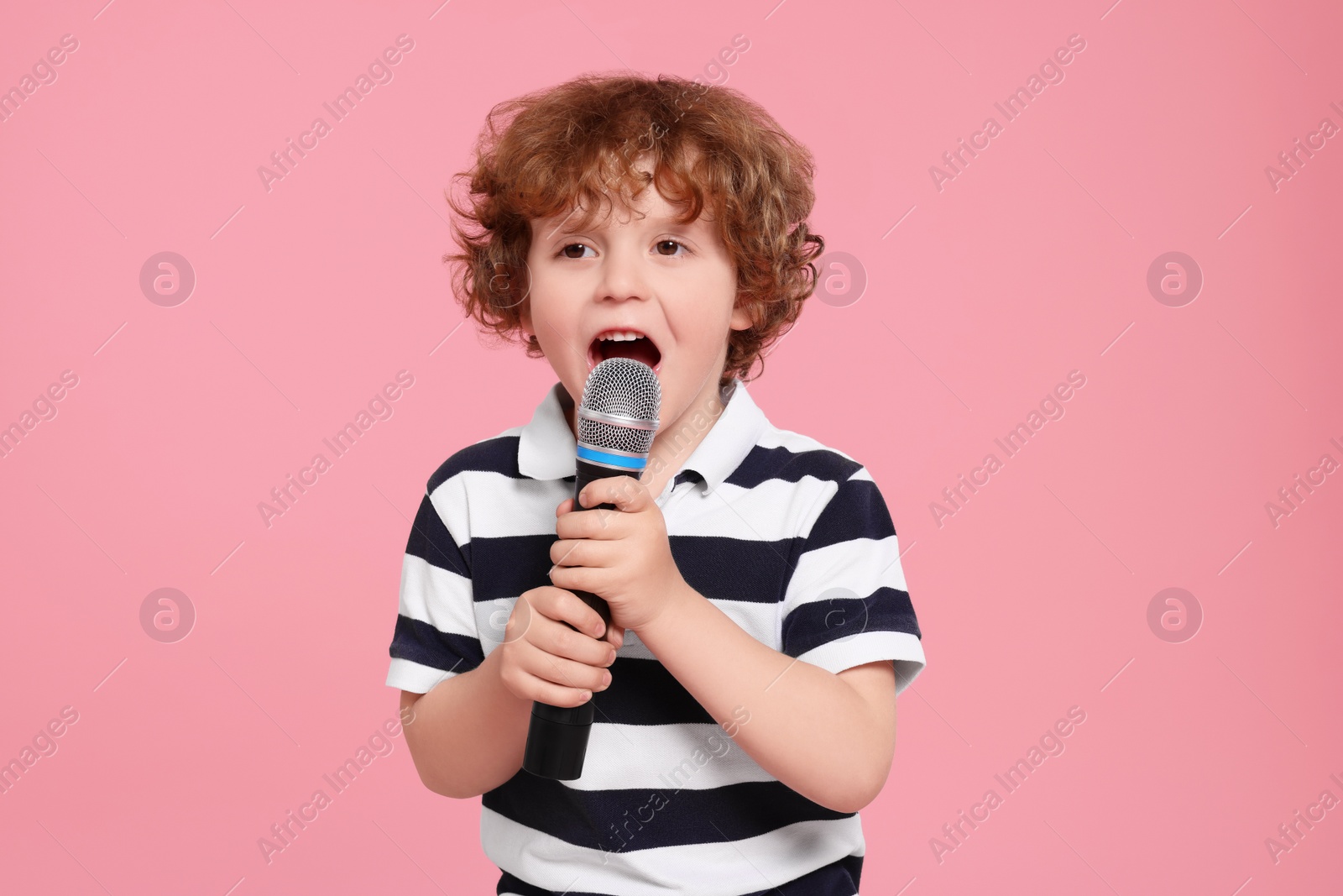 Photo of Cute little boy with microphone singing on pink background