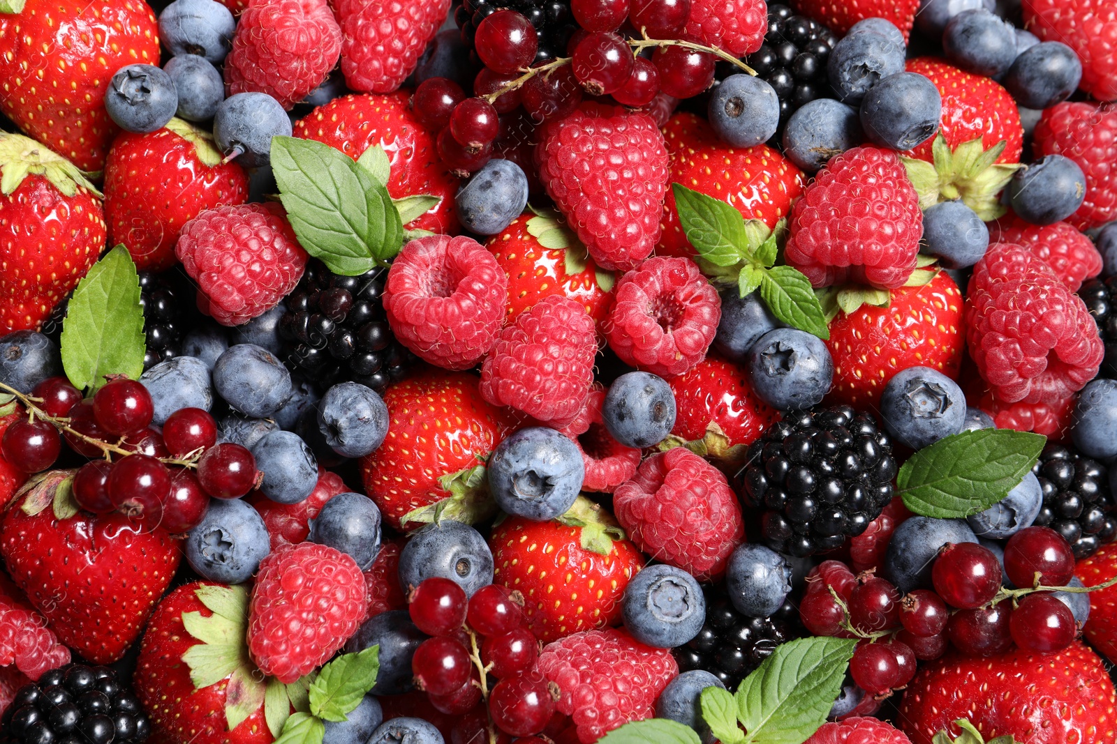 Photo of Assortment of fresh ripe berries with green leaves as background, top view