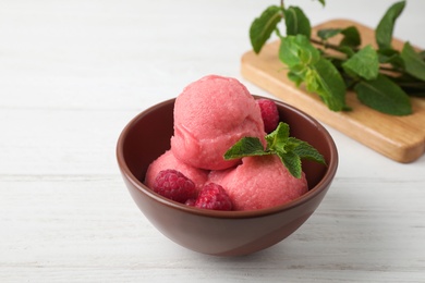 Photo of Delicious pink ice cream served with raspberries and mint in bowl on white wooden table