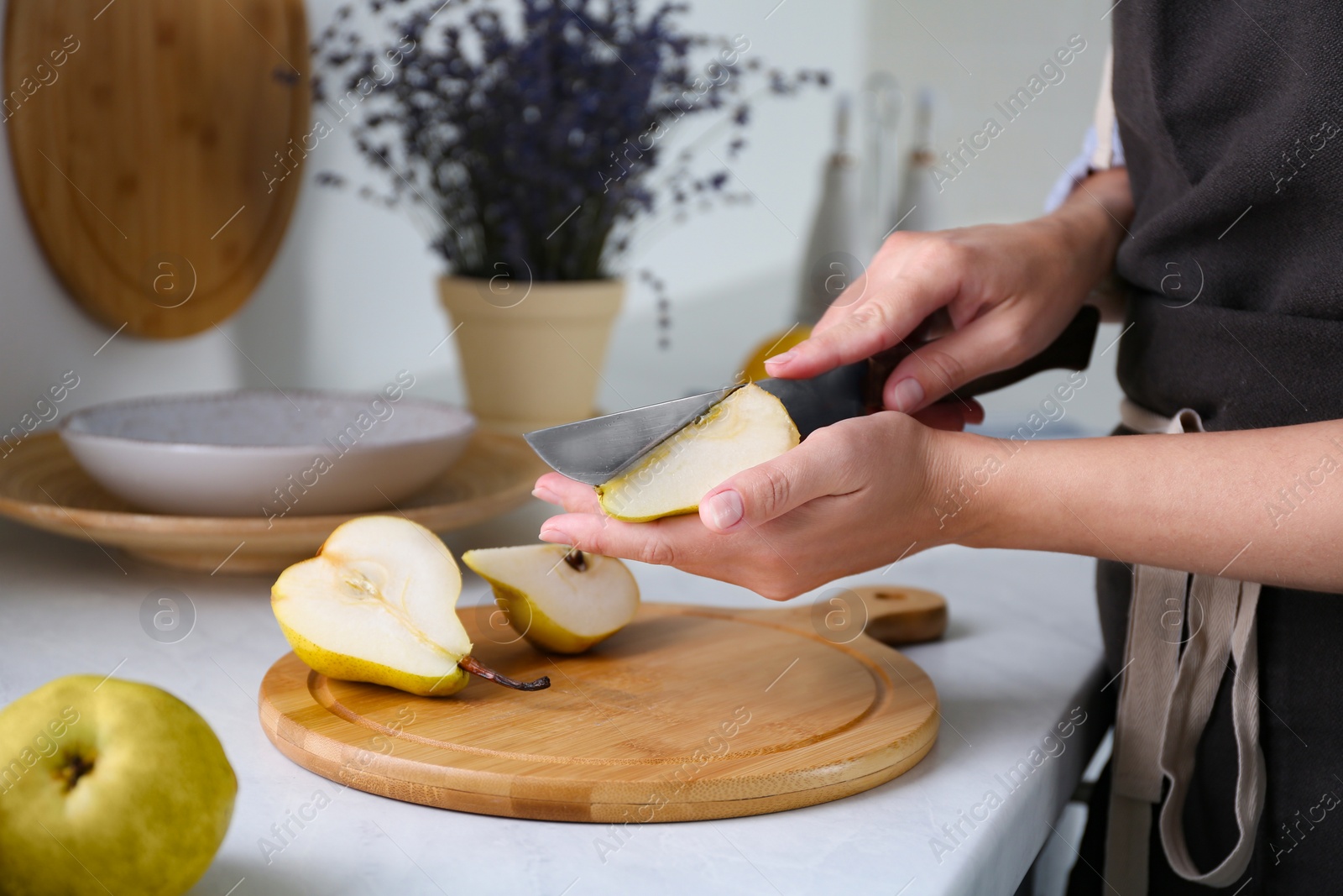 Photo of Woman cutting fresh ripe pear at table in kitchen, closeup