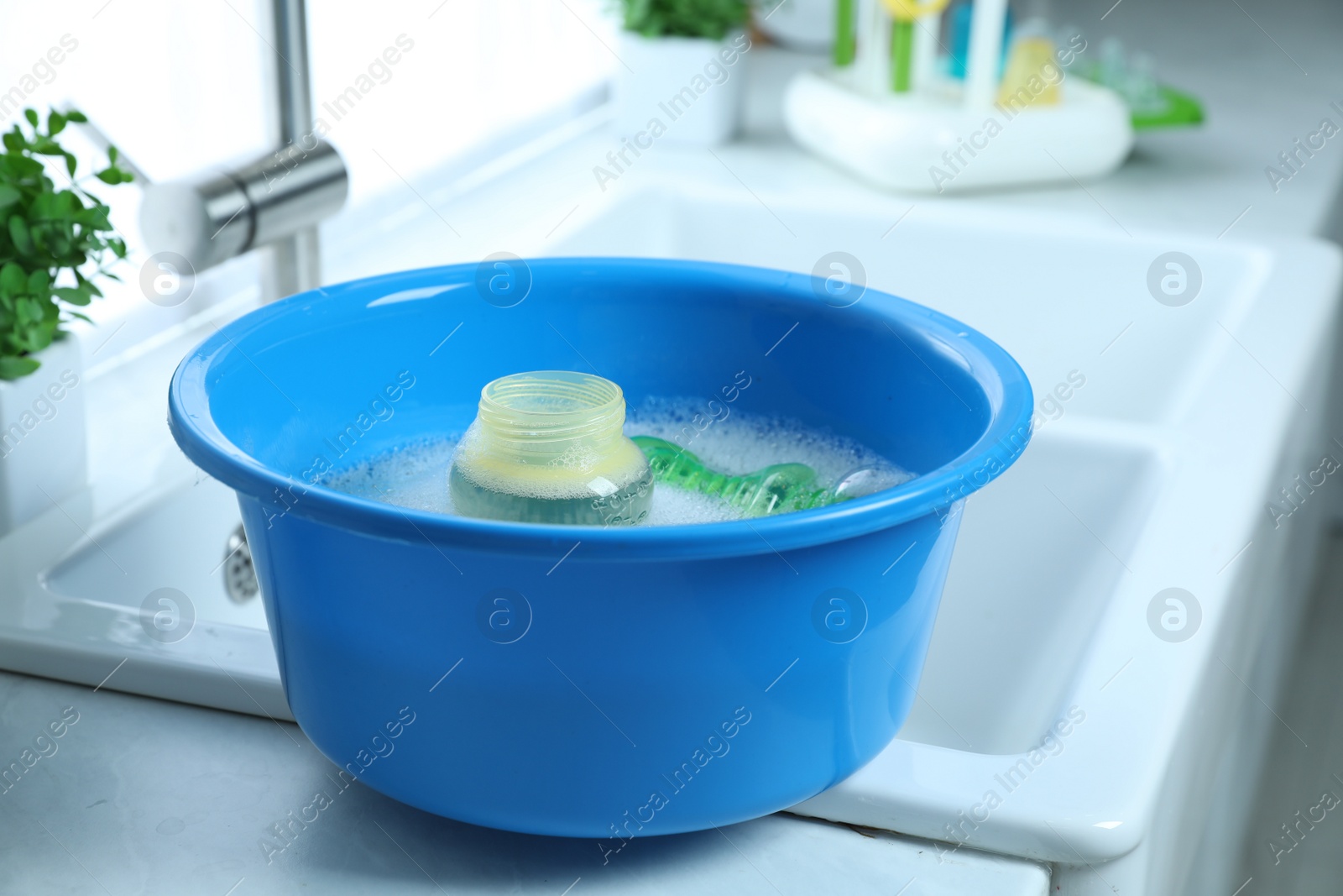 Photo of Light blue basin with baby bottles on white countertop in kitchen