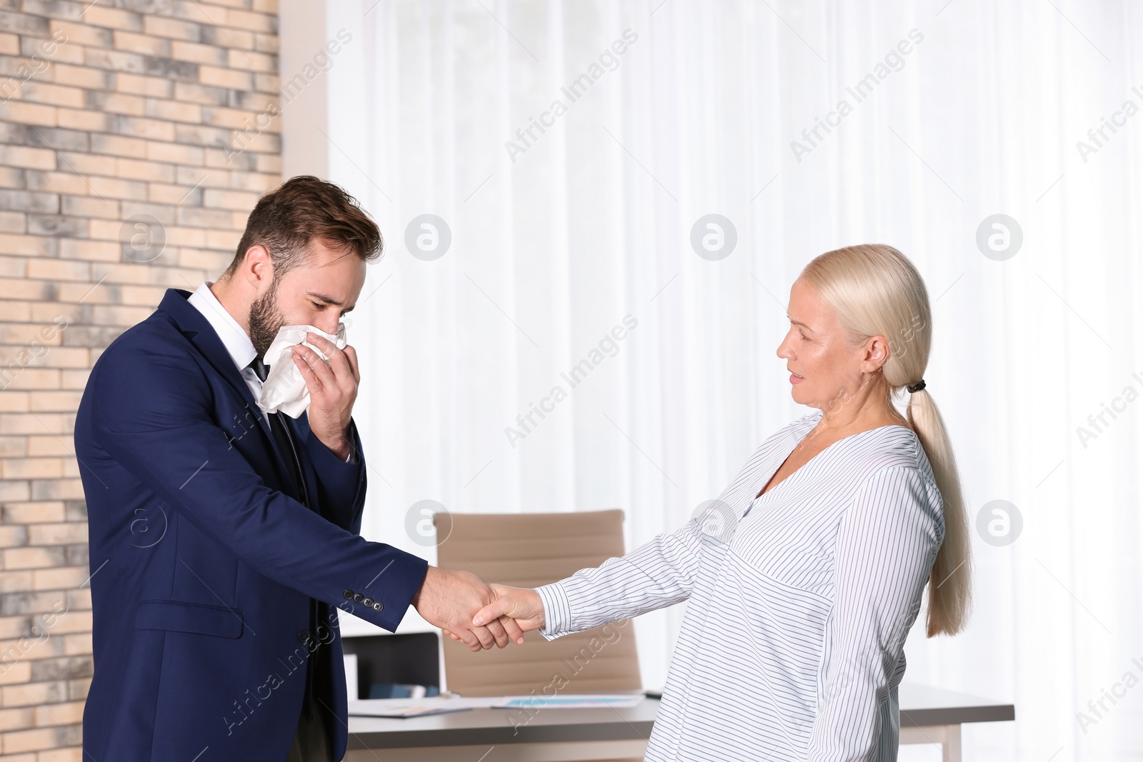 Photo of Mature woman handshaking with ill young man suffering from cough in office