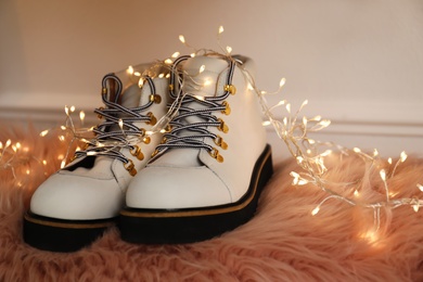 Photo of Pair of stylish female boots and festive lights on fuzzy rug indoors
